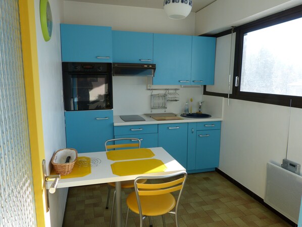 A compact kitchen with blue cabinets, a white countertop, and a dining area with yellow chairs. - Beautiful 2 rooms, Annecy center, located in the golden triangle. (Annecy)