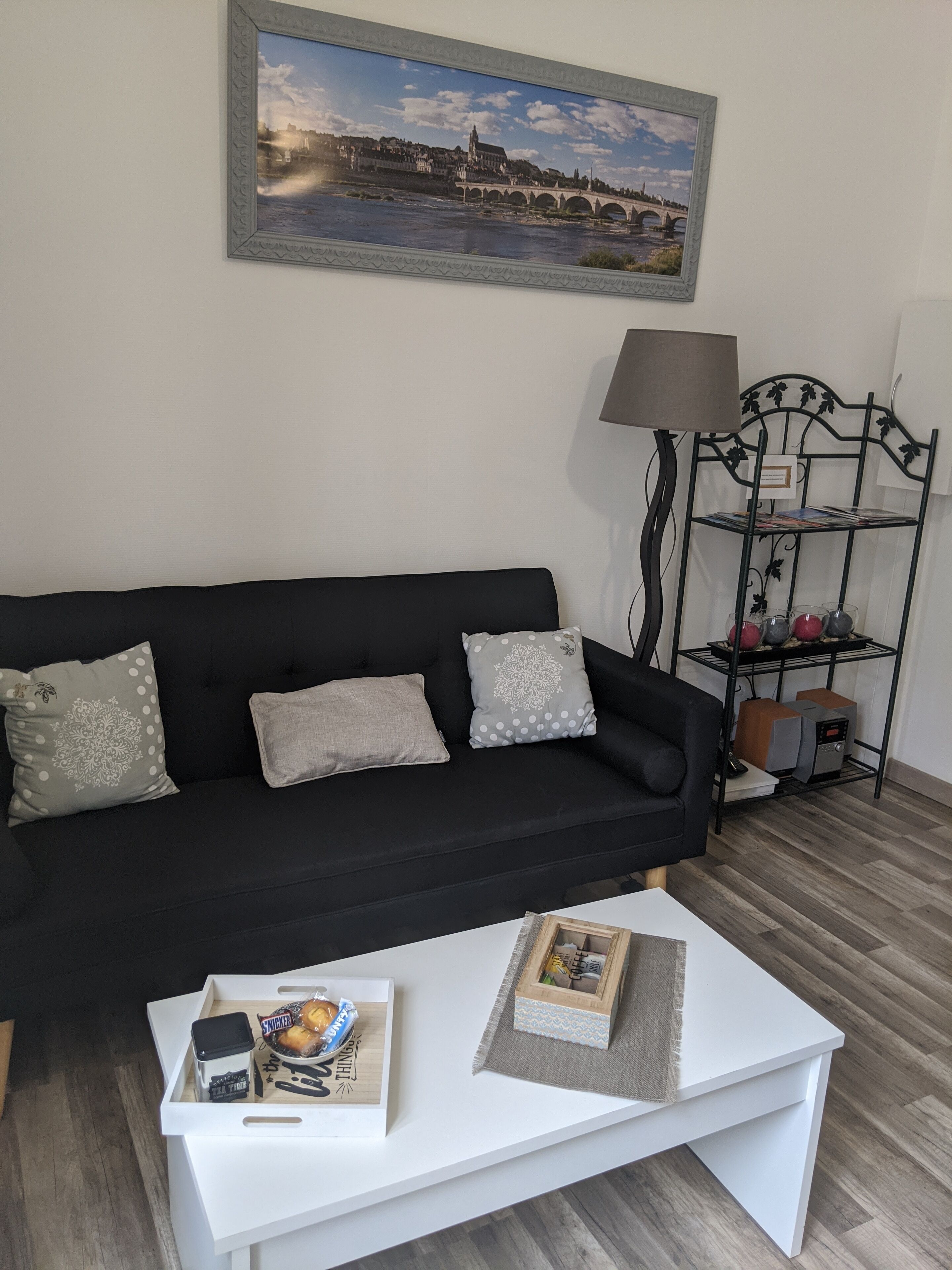 A living room with a black sofa, white coffee table, and a painting of a bridge.