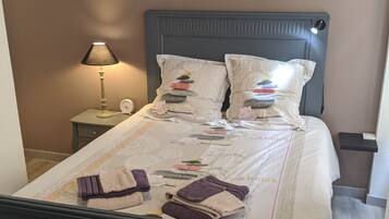 Een netjes opgemaakt bed met een bedspreide met dessin, twee kussens met een steendesign, een bedlampje en een kunstwerk met de tekst 'LOVE'.