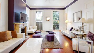 Un salon moderne avec une cheminée, des canapés blancs, des poufs violets et une table basse en verre.
