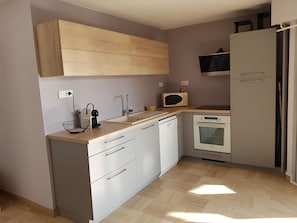 Een kleine keuken met witte kasten, een magnetron, een spoelbak en een vaatwasser.