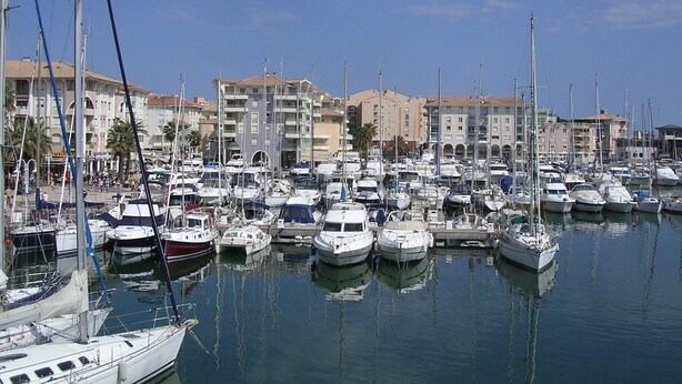 Un port de plaisance où de nombreux bateaux sont amarrés, entouré d’immeubles à plusieurs étages dotés de balcons.