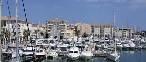 A marina with numerous boats docked, surrounded by multi-story buildings with balconies.