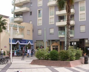 Een meerlaags gebouw met balkons, een centrale binnenplaats met zitplaatsen en een winkel met de naam 'FREQUENCE'.