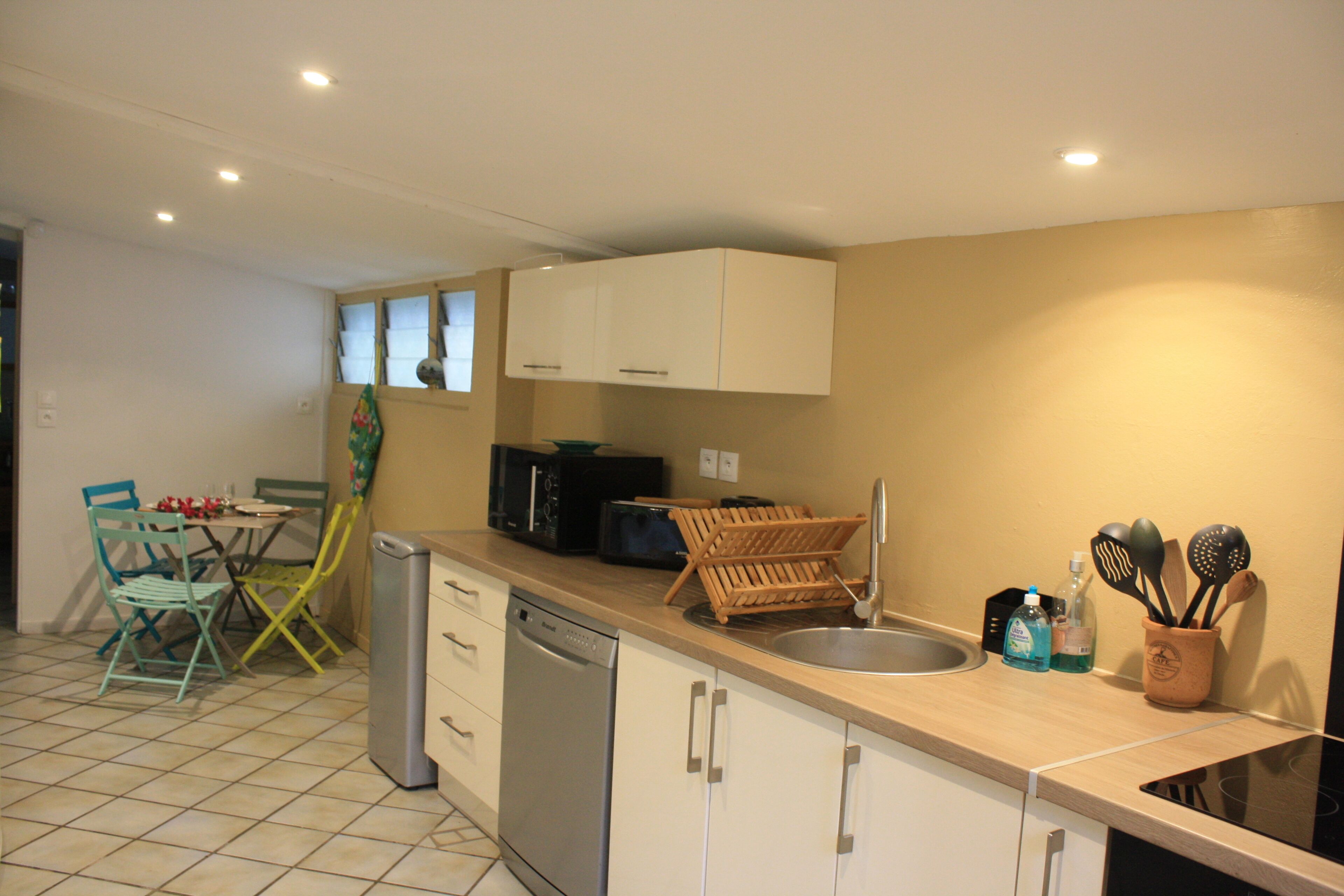 A compact kitchen with a dishwasher, a microwave, and a sink. There are chairs and a table in the adjacent dining area.