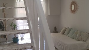 A spacious room with a high ceiling, a staircase, a bed with a patterned bedspread, a wall-mounted decorative mirror, and a small plant. - Jolie CASE CREOLE, LAGON à pied, JARDIN (La Saline-Les-Bains)
