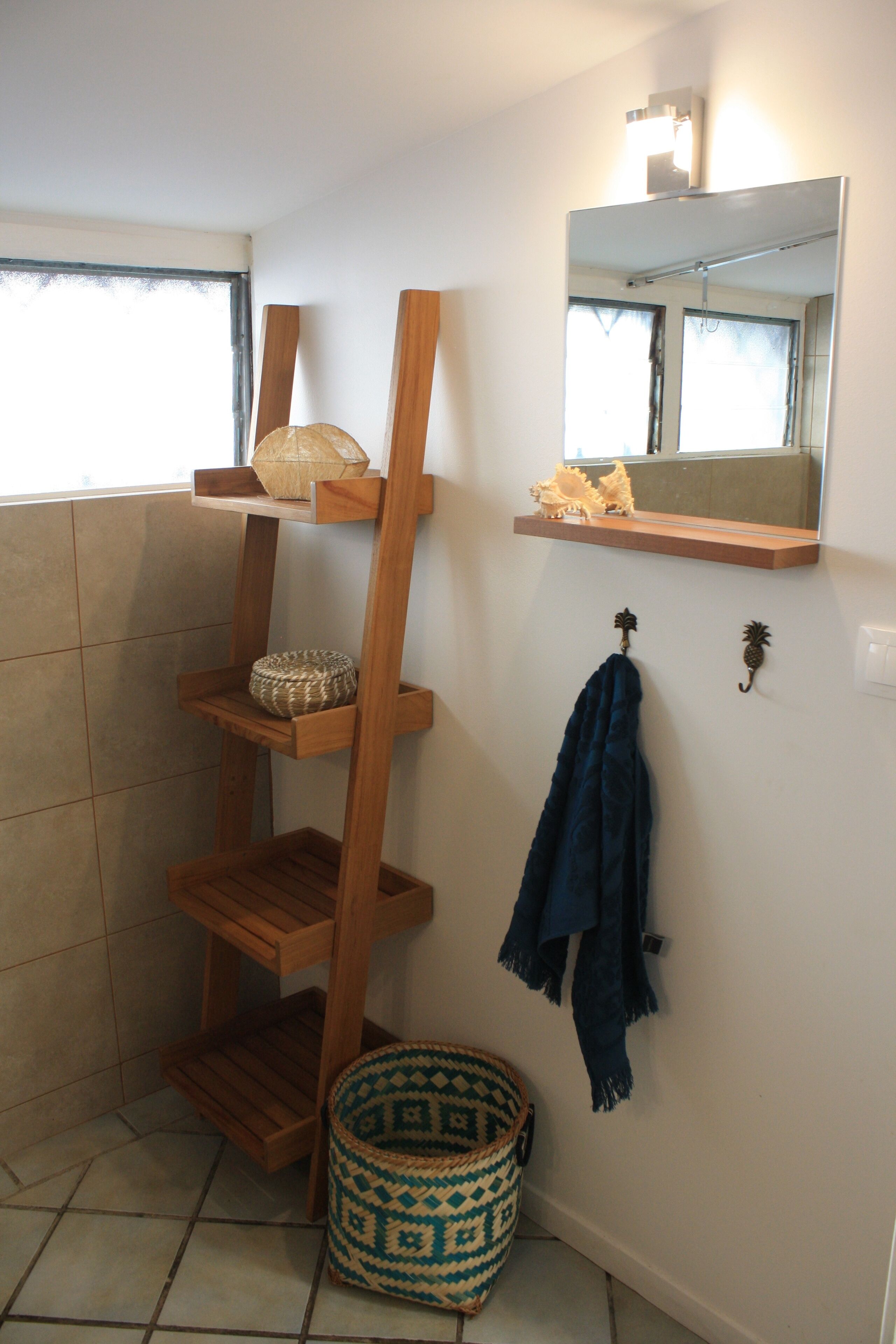 Une salle de bain avec une étagère en bois, un miroir, un porte-serviettes et un panier à motifs.