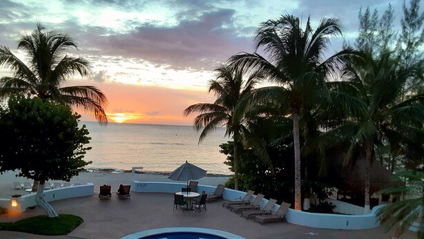 Zona de piscina con sillones de descanso y vista al atardecer sobre el océano.