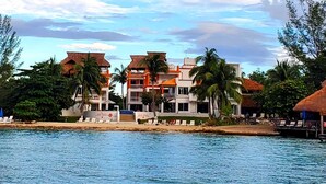 Un hotel frente a la playa con varias edificaciones, palmeras y una vista despejada del océano.
