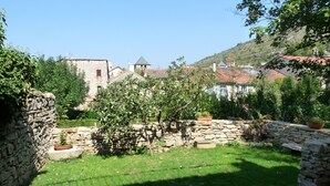 Um pátio com paredes de pedra, uma área gramada e vista para edifícios ao fundo.