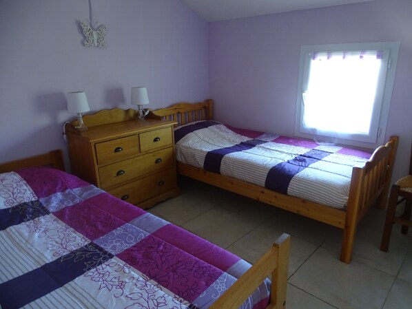 Une chambre avec deux lits simples, une commode en bois, une fenêtre avec des rideaux et une décoration murale représentant des papillons.