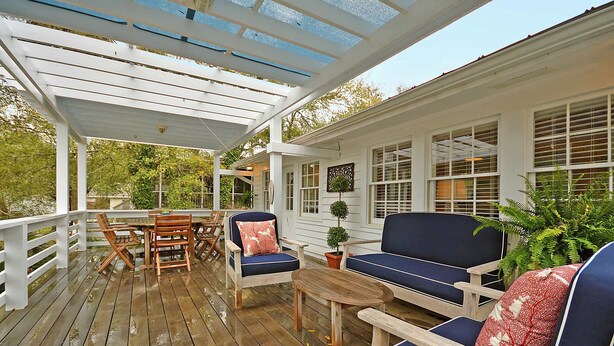 Une terrasse en bois, aménagée avec du mobilier d’extérieur, notamment une table et des chaises, et un espace abrité agrémenté d’une pergola.
