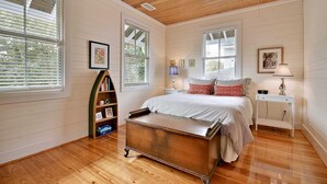 Une chambre à coucher avec un plafond en bois, un lit avec une literie à rayures, une table de chevet avec une lampe et une bibliothèque.