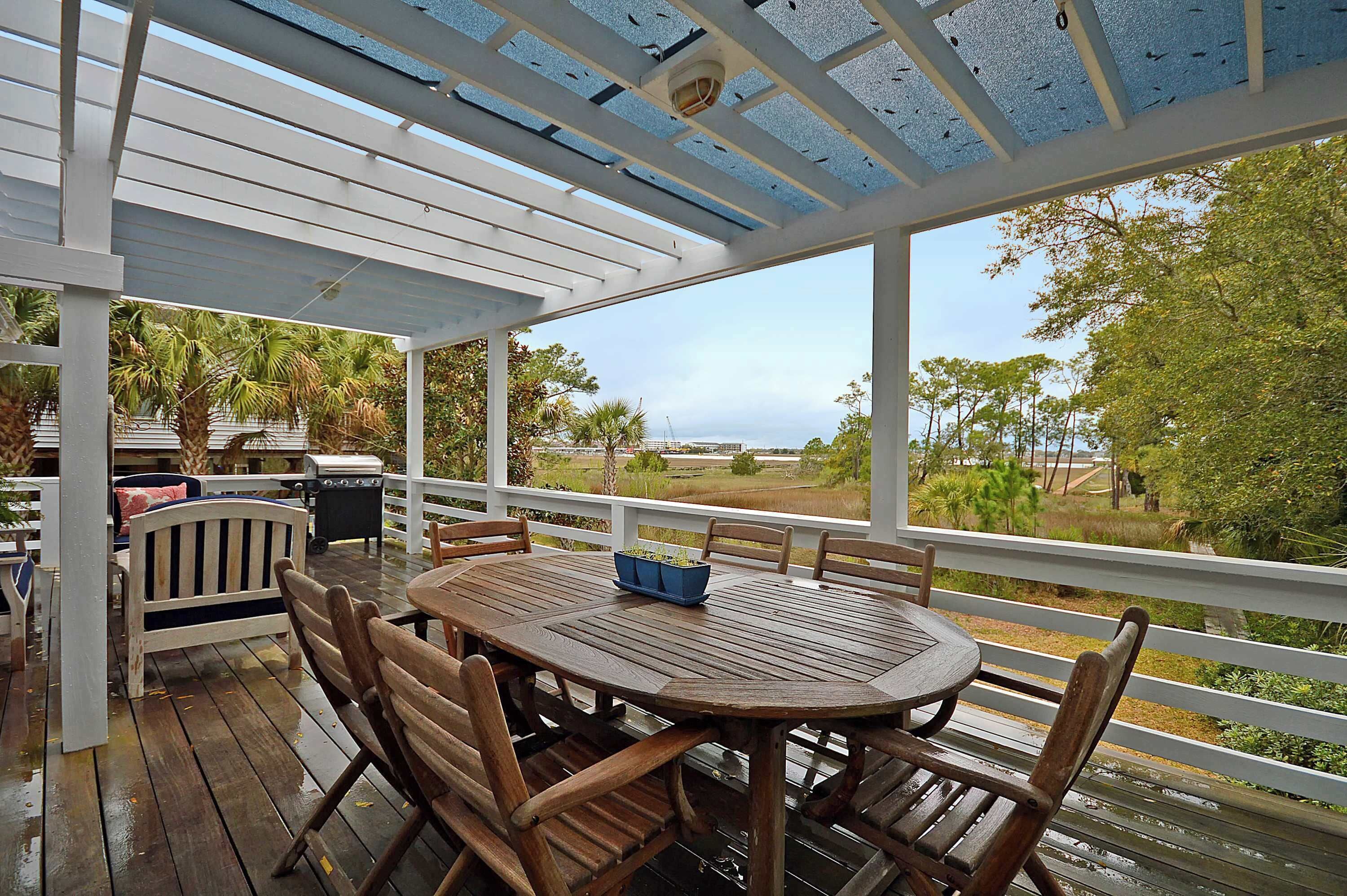 A covered outdoor deck with a wooden table and chairs, a grill, and a view of the surrounding landscape.