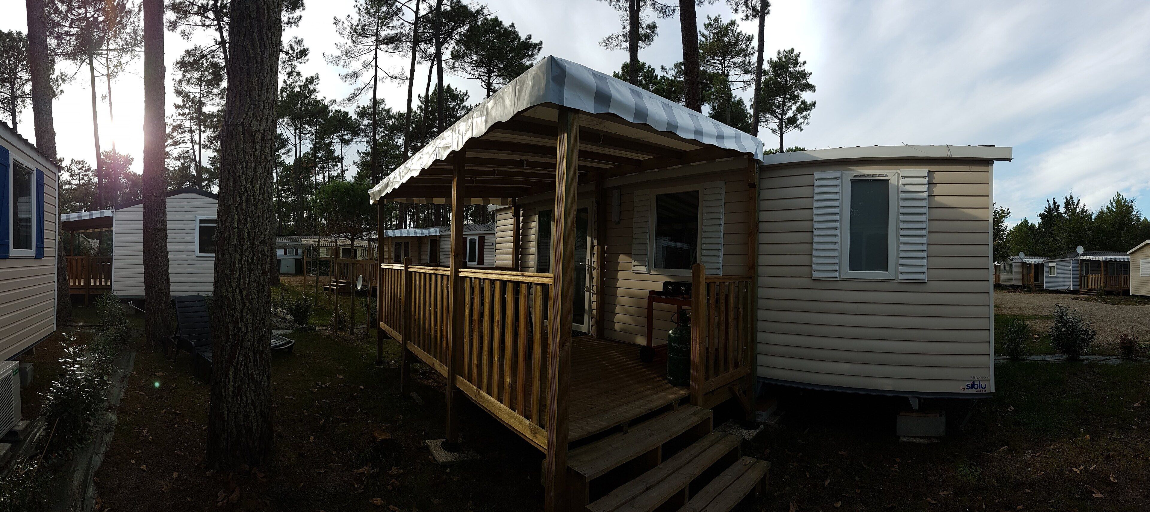 A mobile home with a porch and a covered deck, surrounded by trees.