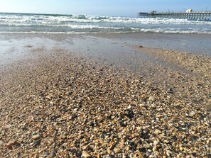 Ein Kiesstrand mit Wellen und einem Pier im Hintergrund.