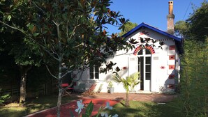 Una casa con techo rojo, una chimenea y un pequeño jardín con flores blancas.