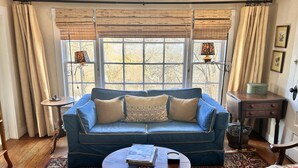 A cozy living room with a blue sofa, a round coffee table, and a patterned rug. - The Best Historic District Victorian Cottage in Eureka Springs (Eureka Springs)