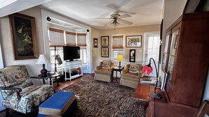 A living room with a television, two armchairs, a sofa, a patterned rug, and a ceiling fan. - The Best Historic District Victorian Cottage in Eureka Springs (Eureka Springs)