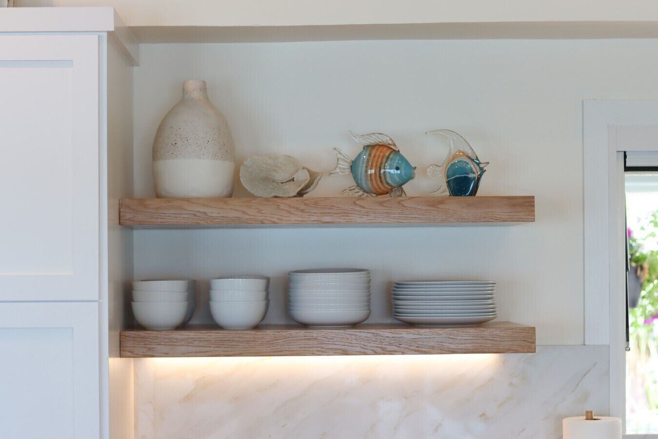 A kitchen with wooden shelves holding white bowls, plates, and decorative items.