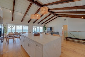 A spacious kitchen with a large island, wooden beams, and a view of the sea.