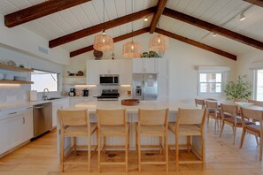 Uma cozinha espaçosa com armários brancos, uma ilha central, cadeiras de madeira e luminárias pendentes.