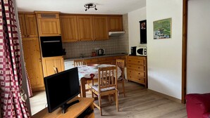A compact kitchen with wooden cabinets, a dining table with chairs, a TV on a wooden stand, and a red chair. - Apartment 4 to 6 people, 52m2, Chatel, Linga, ski Portes du Soleil, MultiPass  (Châtel)