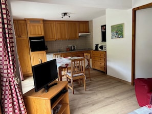 A compact kitchen with wooden cabinets, a dining table with chairs, a TV on a wooden stand, and a red chair. - Apartment 4 to 6 people, 52m2, Chatel, Linga, ski Portes du Soleil, MultiPass  (Châtel)