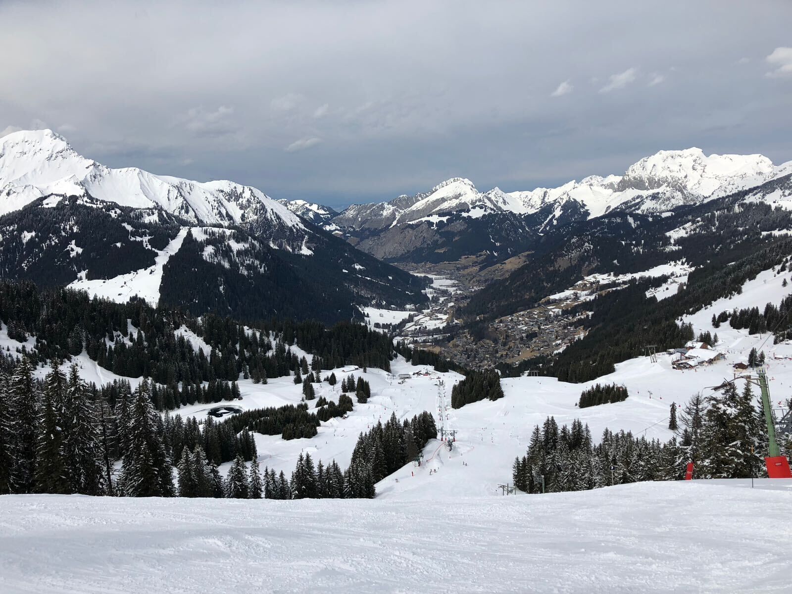 Paisagem montanhosa coberta de neve, com pistas de esqui e uma cidade no vale.