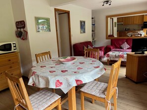 A dining area with a round table, chairs, and a bowl. There is a kitchen in the background with wooden cabinets and a microwave. - Apartment 4 to 6 people, 52m2, Chatel, Linga, ski Portes du Soleil, MultiPass  (Châtel)