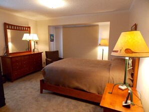 Relax in this inviting space with a comfortable bed, dresser, and nightstand, plus a window with blinds and a wall-mounted mirror.