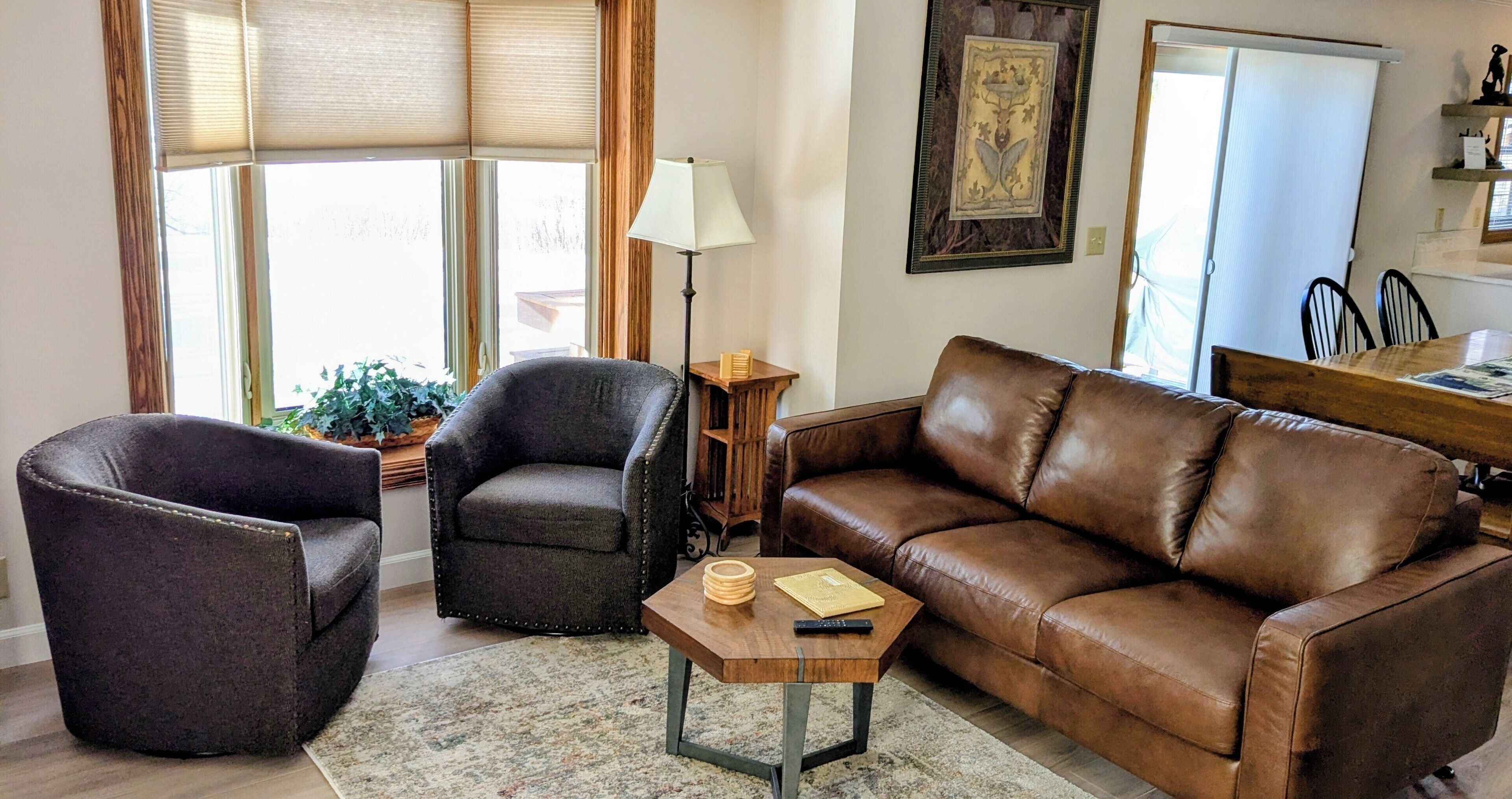 Ein Wohnzimmer mit einem braunen Ledersofa, zwei Sesseln, einem kleinen Holztisch und einer Stehlampe.