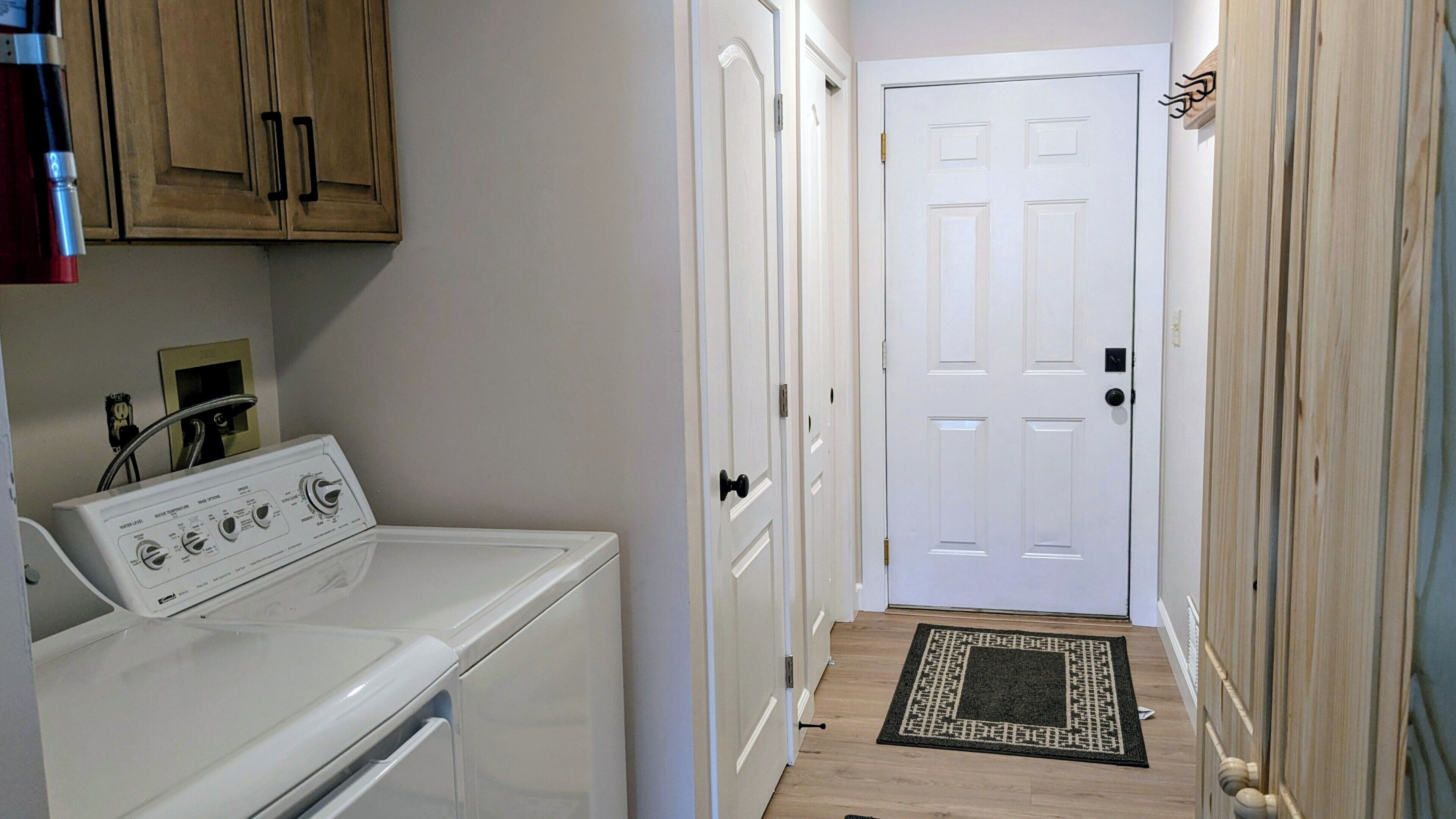 A laundry area with a washing machine, a door, and a wooden floor.