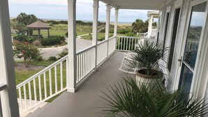 A covered porch with white railings, a view of the beach, and a gazebo in the background.