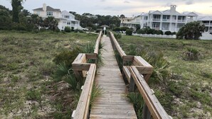 A wooden boardwalk leading to a row of white beachfront houses with balconies.