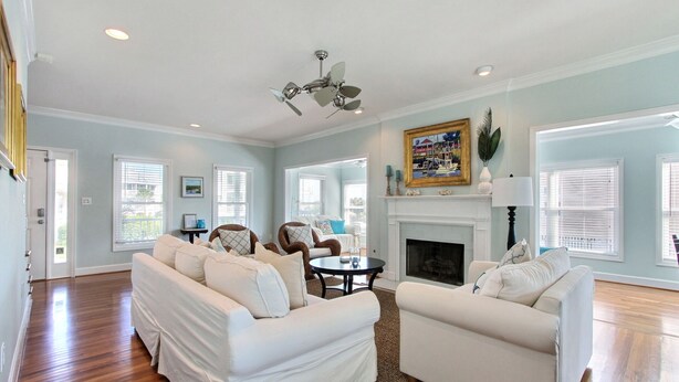 A spacious living room with two white sofas, a fireplace, and a ceiling fan.