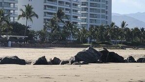 A beachfront hotel with multiple floors, palm trees, and a rocky shoreline. - Luxurious newly renovated BeachFront Condo & Vidanta Membership (Nuevo Vallarta)