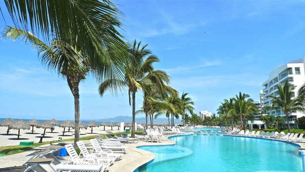 A pool area with lounge chairs and palm trees, surrounded by a building with balconies. - Luxurious newly renovated BeachFront Condo & Vidanta Membership (Nuevo Vallarta)
