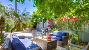 Une terrasse dotée de meubles en osier, d’un barbecue et d’une végétation luxuriante.