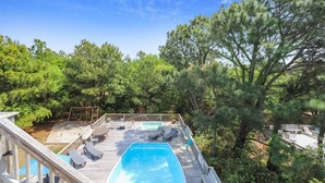 Una terrassa de fusta amb una piscina, gandules i vistes a una zona boscosa.