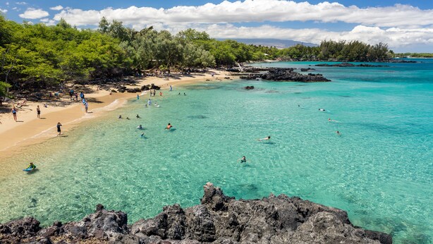 Une plage à l’eau turquoise et limpide, bordée d’un rivage rocheux et d’une végétation luxuriante.
