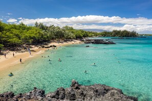 A beach with clear turquoise water, rocky shore, and lush greenery.