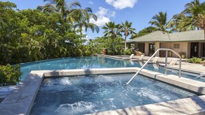Une piscine avec un jacuzzi, entourée de palmiers et bordée d’un bâtiment dont le toit est recouvert de tuiles.