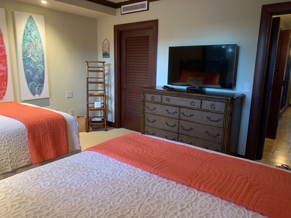 A hotel room with two beds, a wooden dresser, a television, and a surfboard art piece on the wall.