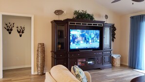 A living room with a dark wooden entertainment center, a flat-screen TV, and a potted plant on top. - Walk to Lake Sumter Landing! Golf cart included! (The Villages)