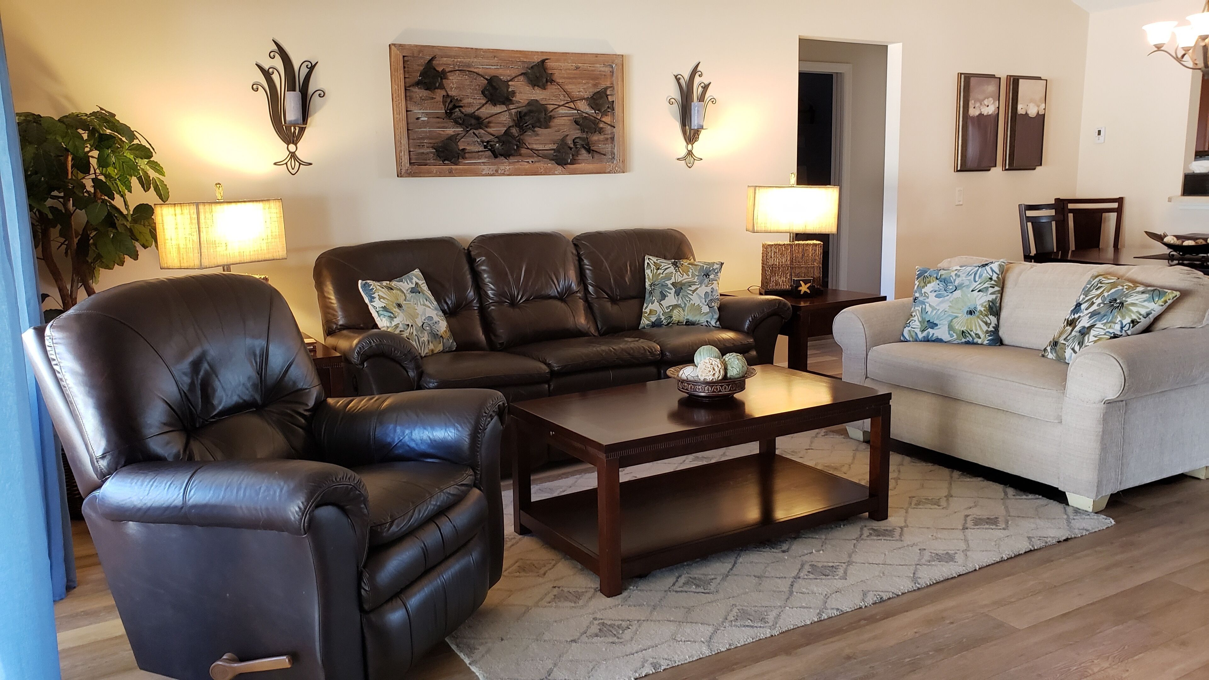 A living room with a brown leather sofa, a beige sofa, a wooden coffee table, and two wall-mounted lamps.
