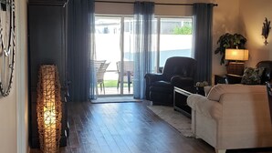 A spacious living room with a wooden floor, a ceiling fan, a sofa, a coffee table, and a dining area with chairs. - Walk to Lake Sumter Landing! Golf cart included! (The Villages)