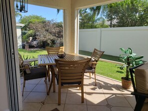 Een terras met een tafel en stoelen, een bloempot en uitzicht op een verzorgd gazon en bomen.