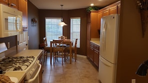 A compact kitchen with a gas stove, white refrigerator, wooden cabinets, and a dining table with chairs.