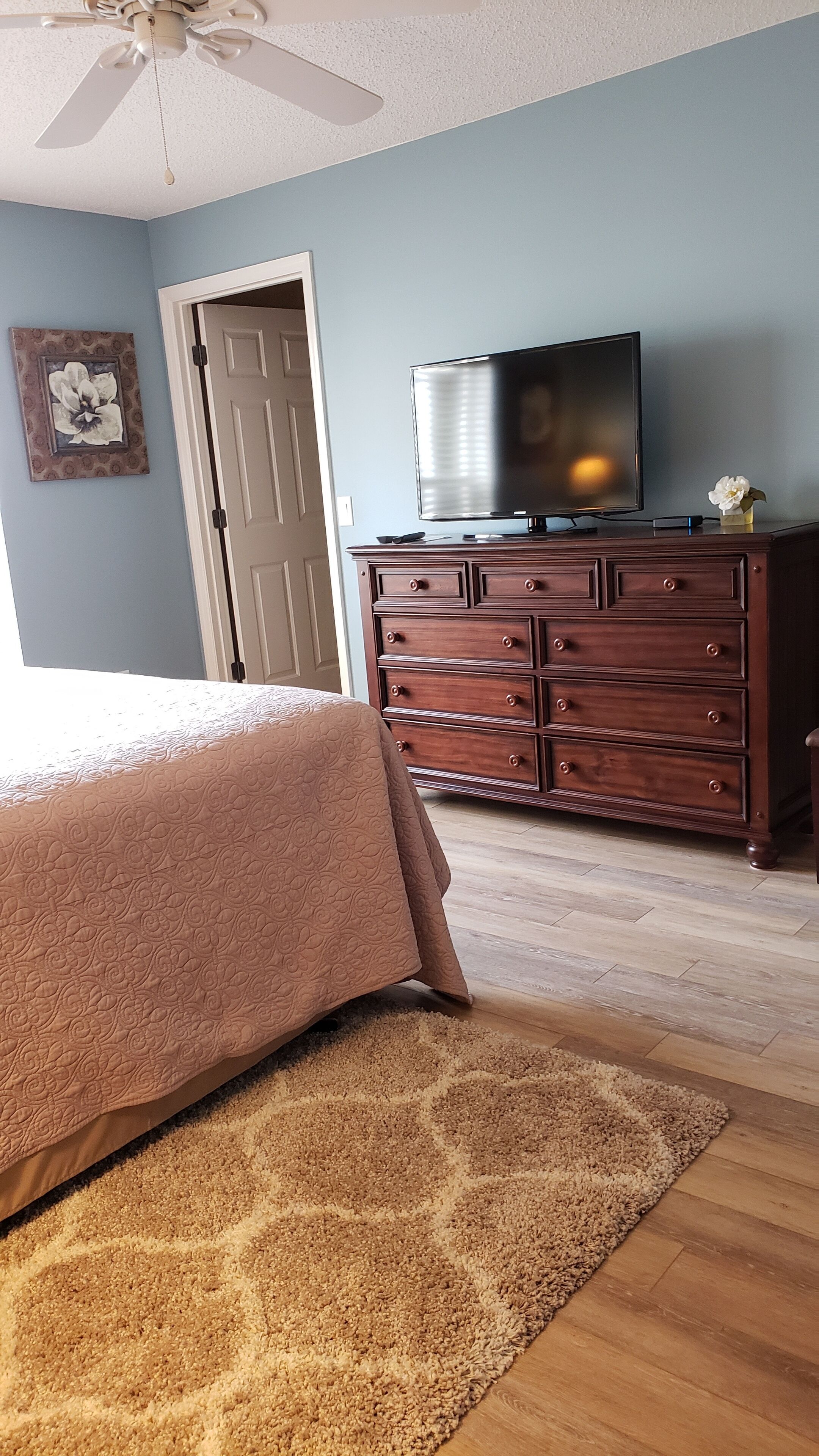 Une chambre à coucher comprenant un lit, une commode, un téléviseur et un ventilateur de plafond.